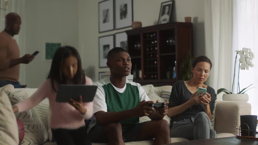 A group of people walk over to the couch using cell phones