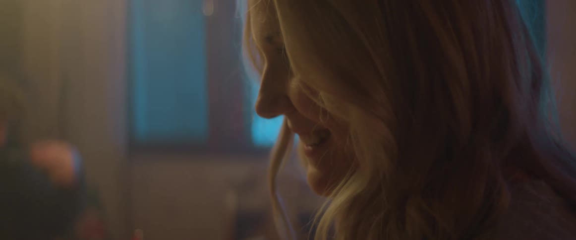 Blonde woman standing indoors talking to someone while her husband is nearby
