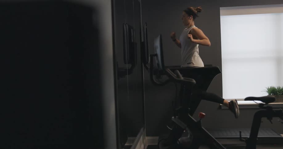 Woman with black headband gray sport shirt and black leggings does exercise on treadmill in the gym