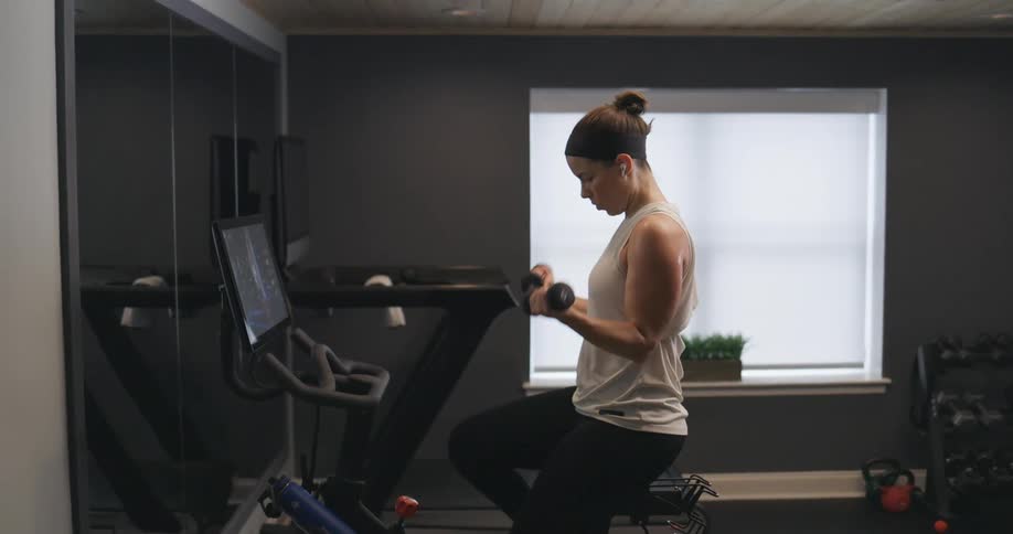 Woman using hand weights while pedaling on stationary bike at her home gym