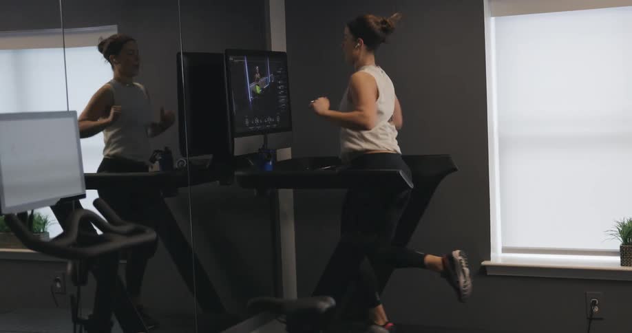 Woman with black headband gray sport shirt and black leggings does exercise on treadmill in the gym