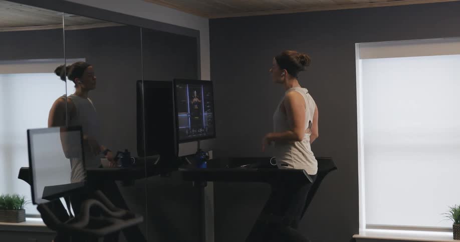 Woman with black headband gray sport shirt and black leggings does exercise on treadmill in the gym