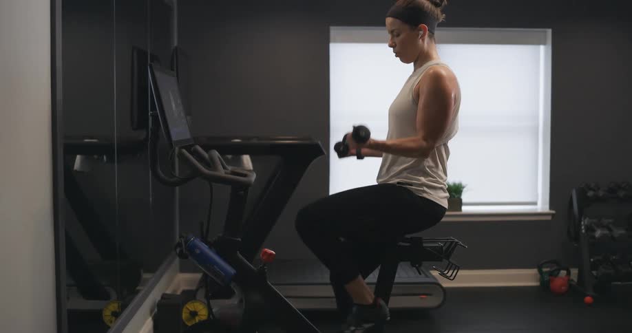 A woman is lifting weights and walking on a treadmill