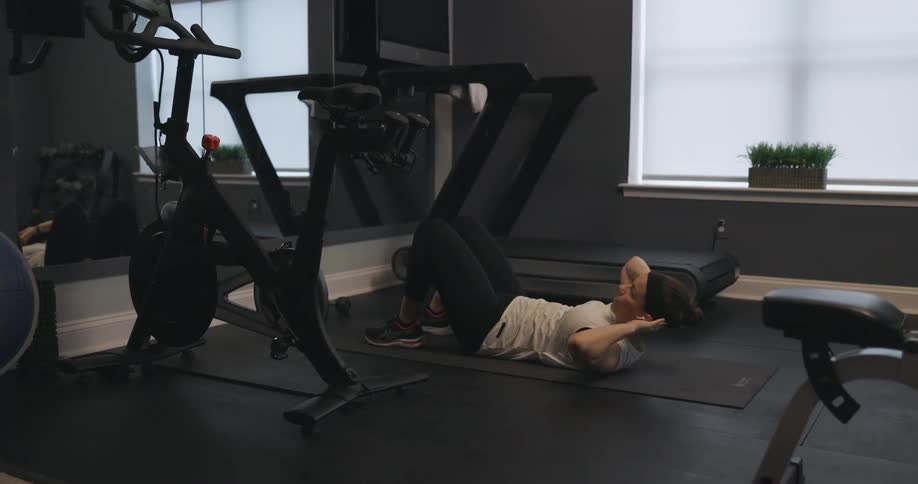 A woman does elbow to knee crunches on a mat in a gym