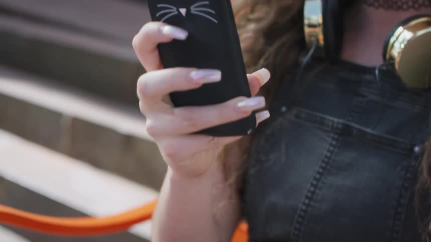 A teenage girl is sitting on a bench outdoors and texting with her phone