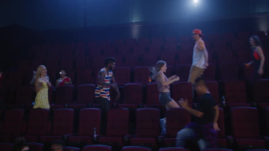 Multiple people run and dance in the theater seats