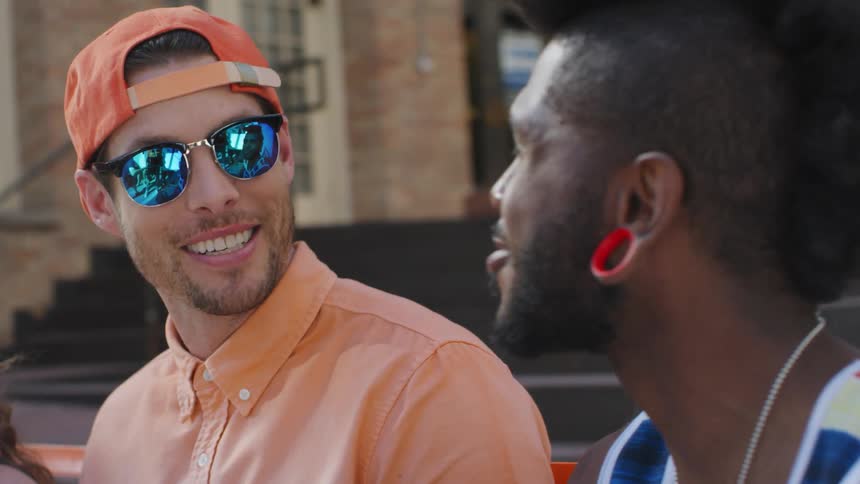 Two young men laugh and talk with one another while sitting together on a bench outdoors during the day