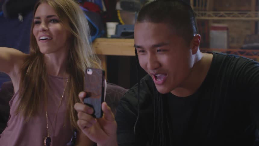 Man and woman sitting on the couch dancing and laughing while recording with a smartphone