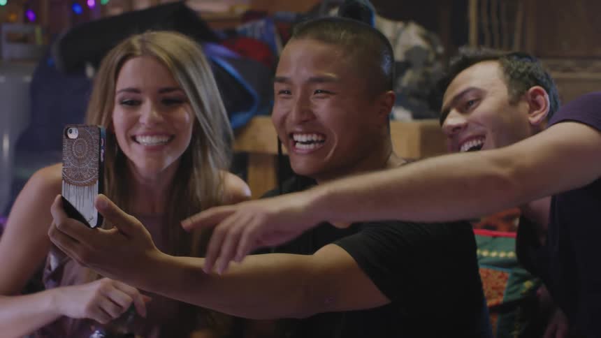 Three friends sitting in a couch having a good time video chatting with someonen else on a smartphone
