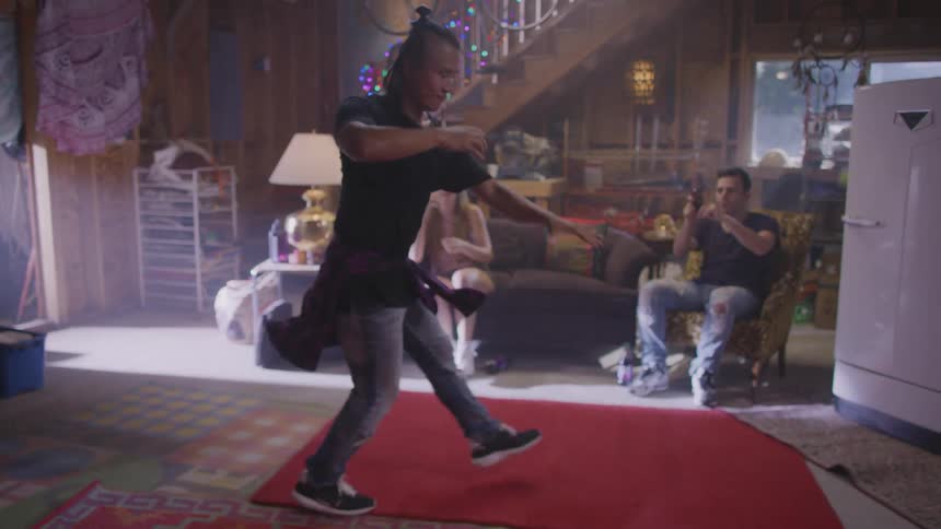 An Asian man is dancing while someone plays drums and his friends cheer