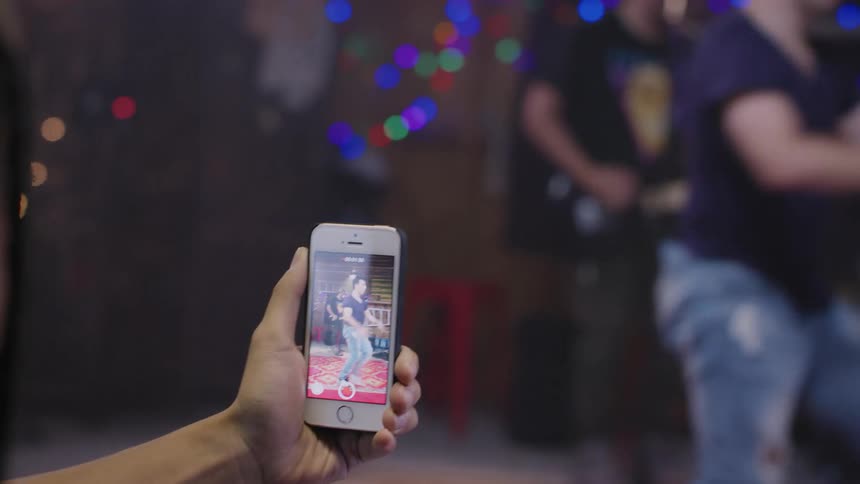 Man using his smartphone to record a man breakdancing and another man behind him playing guitar