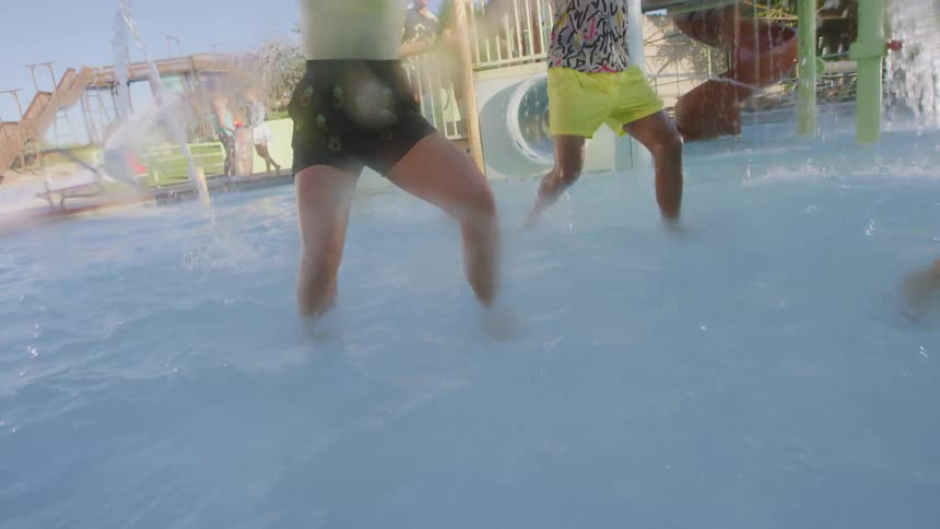 Teenagers dancing in the water at a water park as others watch and dance in the background