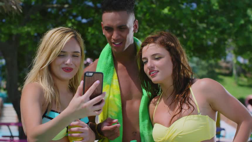 Three young friends in swimwear use a smartphone on a sunny day