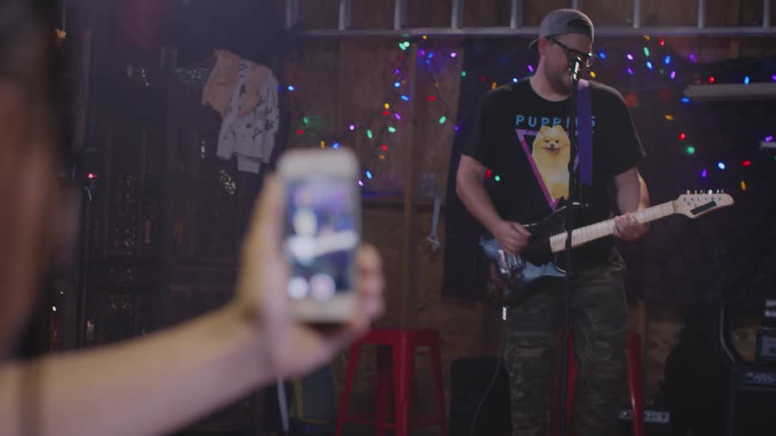 A woman uses her smartphone to record a musician on stage