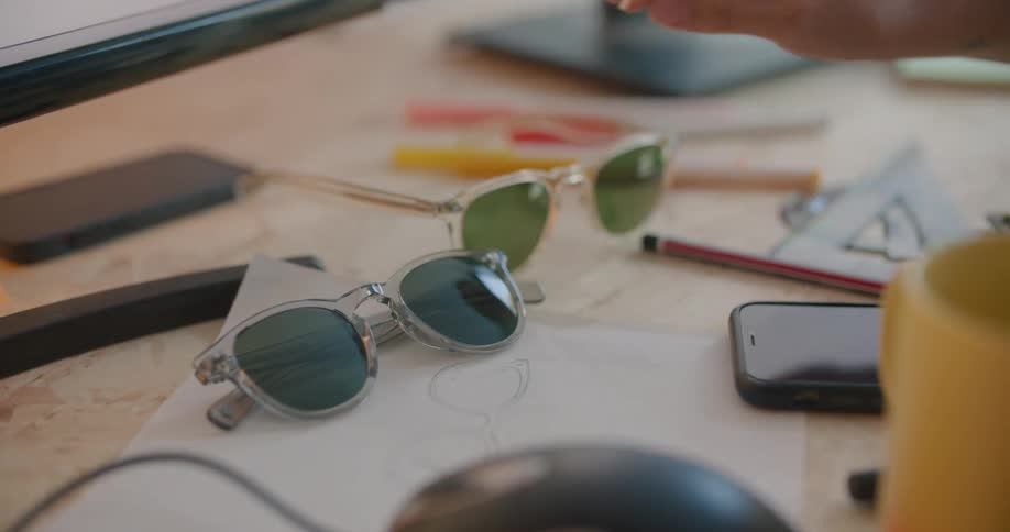 A person lifts sunglasses from the desk