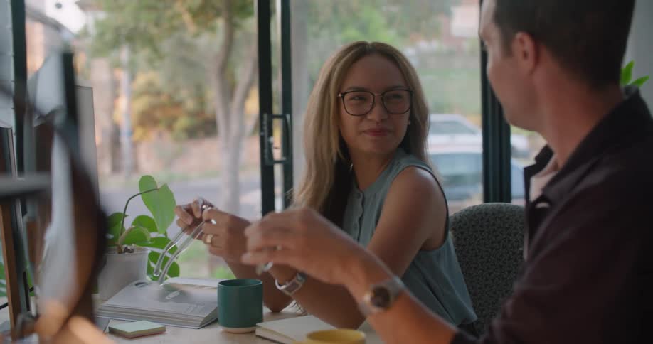 Two coworkers talk to each other and laugh while both are holding stylish sunglasses