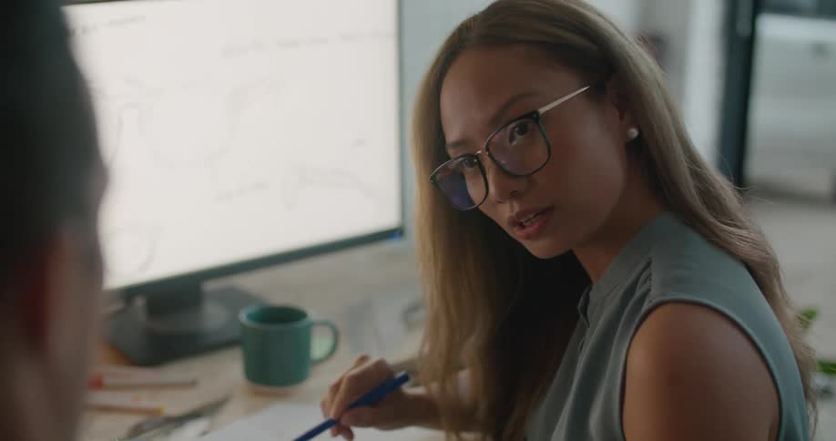 Woman and man sitting at the office desk talking and writing on a notebook