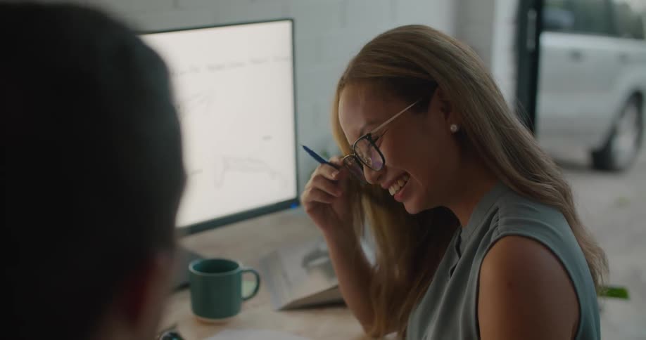 Coworkers smile as they work at desk withmonitor