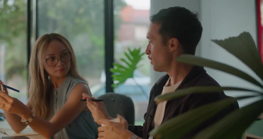Man and woman sitting at their office desk in front of a laptop and a computer while talking about a sunglasses