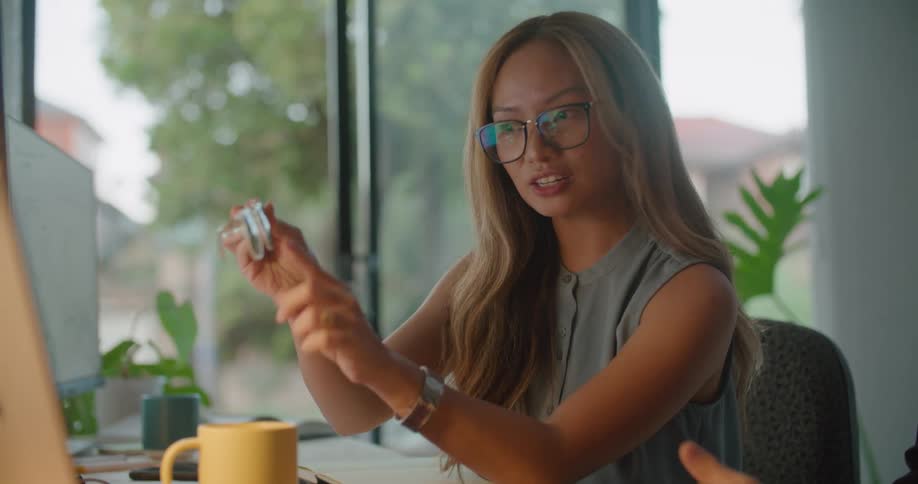 Woman sitting at the office desk on a video call on her laptop showing a sunglasses to the camera