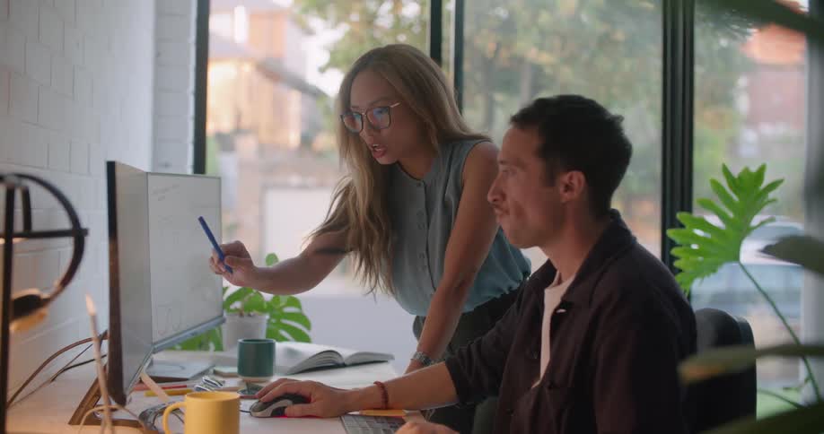 A woman talks to a man as he types on the computer