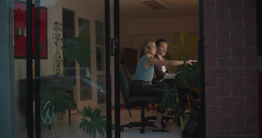 Man and woman sitting at the table in a office talking and pointing at the screen