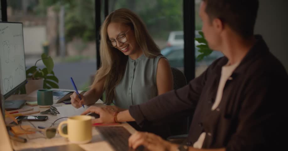 Woman slides across the room on a chair while holding a piece of paper then talks with a man sitting at a desk
