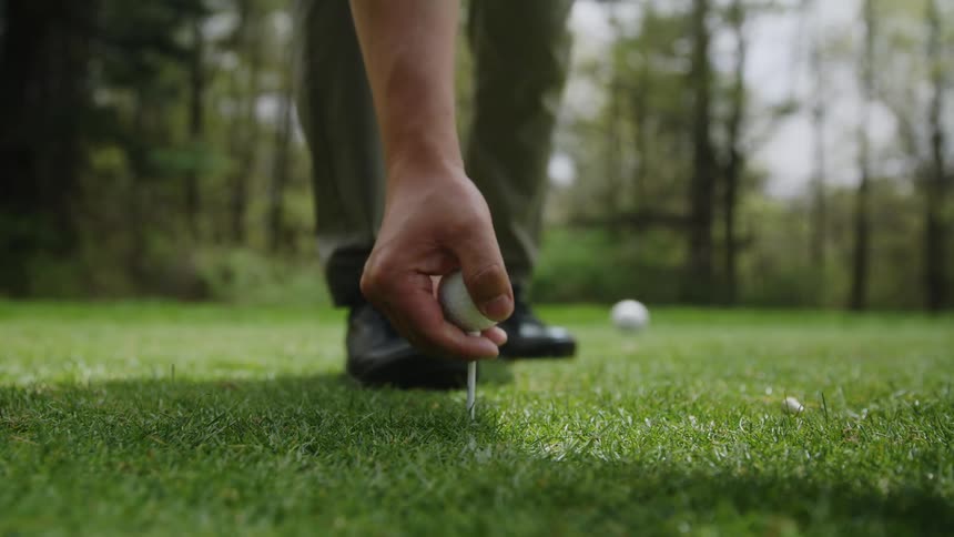 A golfer places a ball and tee into the grass then gets ready for his shot