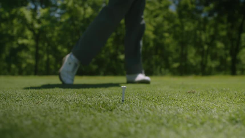 A person hitting a golf ball with a golf club in a golf field at a sunny day