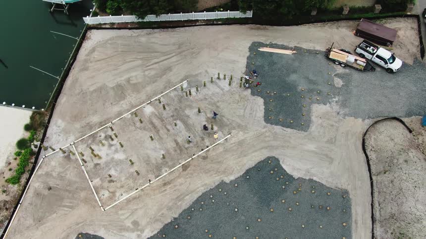 Aerial of truck and trailer parked on a lot as workers work on construction site nearby