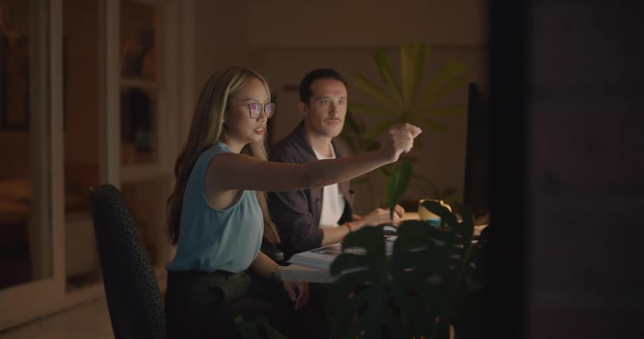 Woman and man sitting at a table and using a computer while talking and then they high five each other