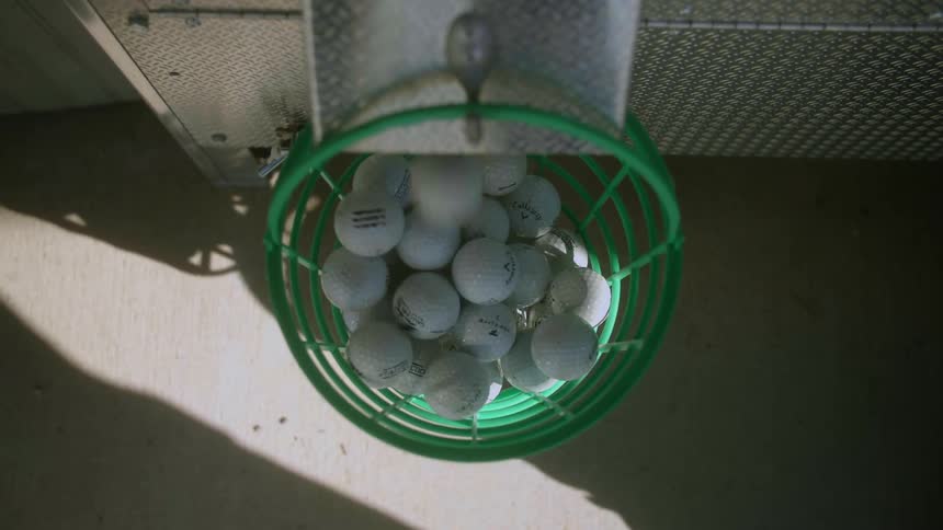 A person waits for golf balls to fall out of a tube and fill and bowl