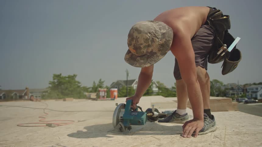 Man uses a skill saw to cut the pressed board outside on a hot sunny day