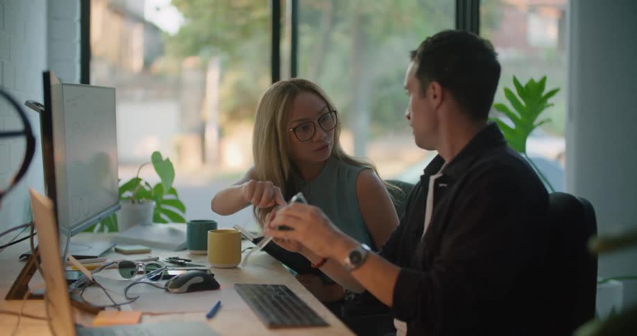 Colleagues discuss the design of a pair of sunglasses while sitting at their desks