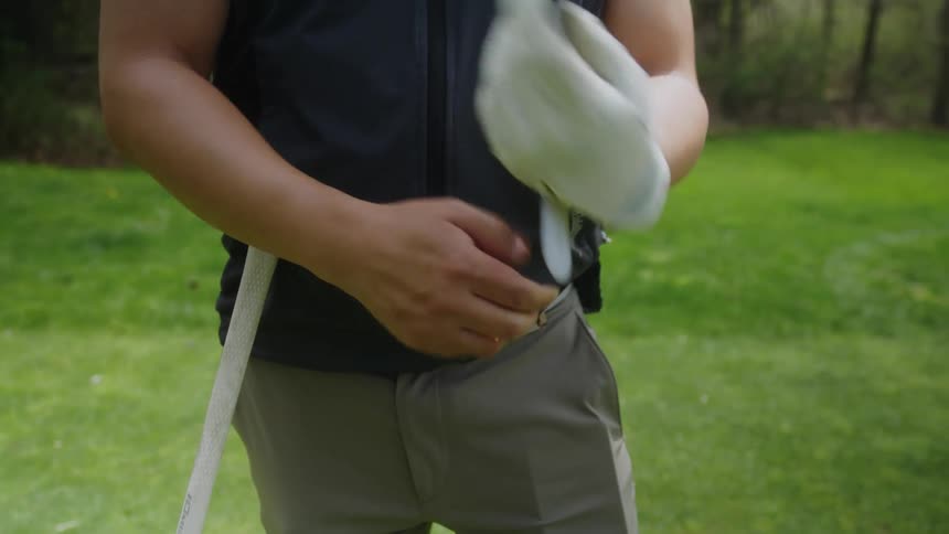 Man putting on a golf glove while standing at a golfing field at a sunny day