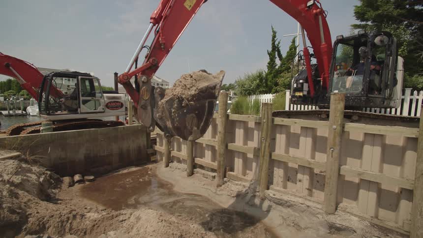 Excavator digs a foundation on a construction site as a man watches