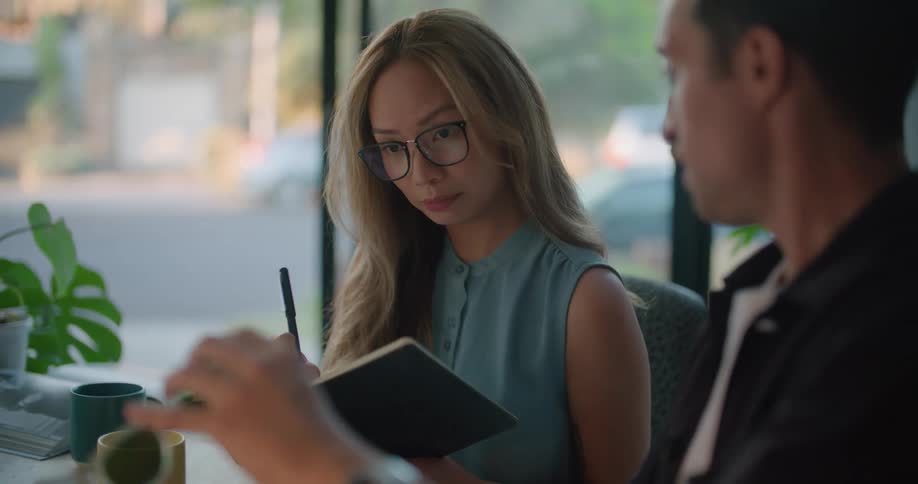 A woman takes notes while discussing the design of a pair of glasses with a colleague