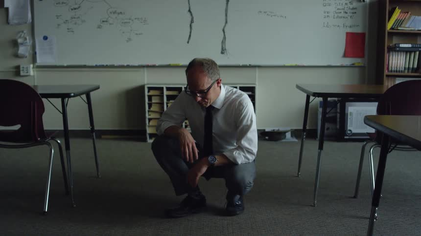 Teacher wearing formal clothes crouching in front of the whiteboard of an empty classroom
