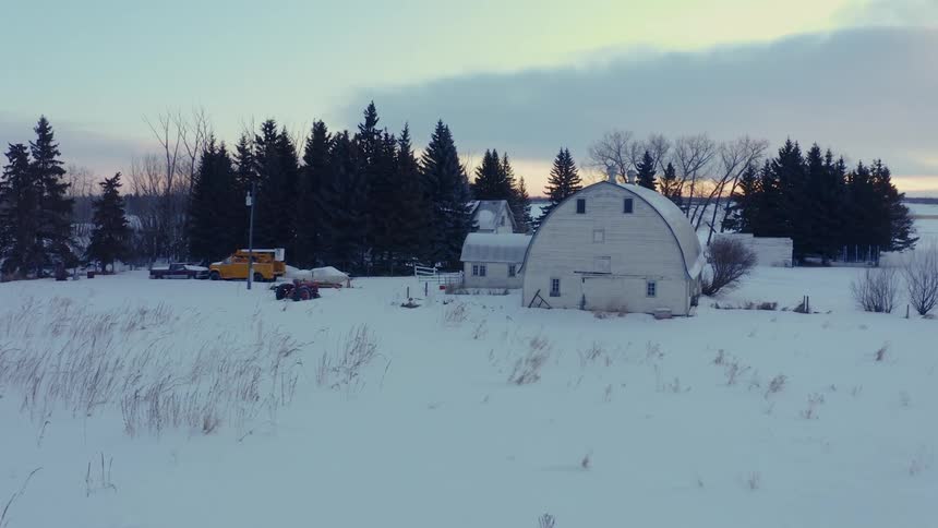 Snow covers farmhouse and stretches to forest on the horizon