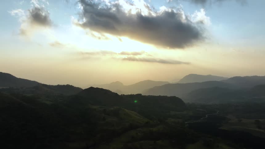 River runs through valley passing hills toward fog covered mountains near the red tinted horizon