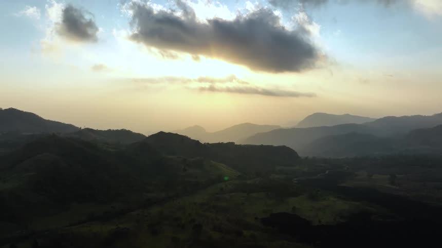 Trees and grass along a mountain ridge and silhouettes of mountains on the horizon under a cloudy sky