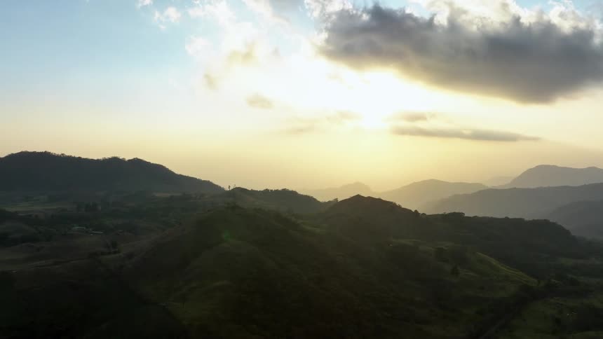 Trees and grass along a mountain ridge and silhouettes of mountains on the horizon under a cloudy sky