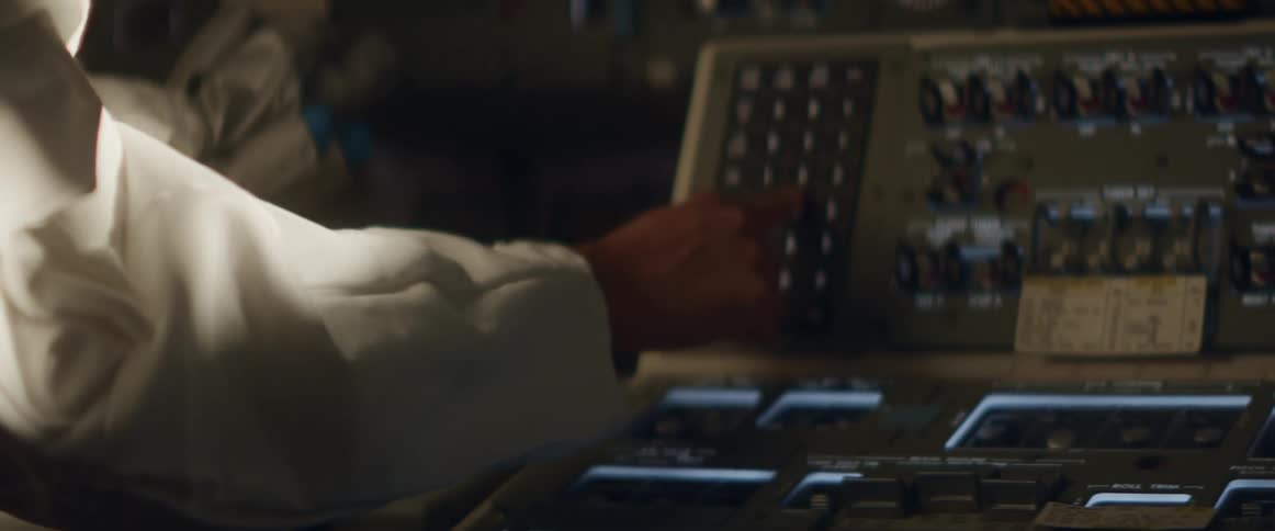 Person wearing astronaut suit adjusts buttons in cockpit after removing their gloves