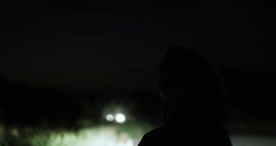 A woman is standing at night on a dirt road
