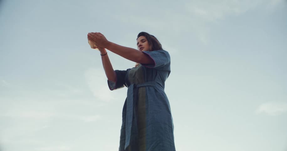 Woman stands outdoors letting dust trickle and into the wind from her cupped hands