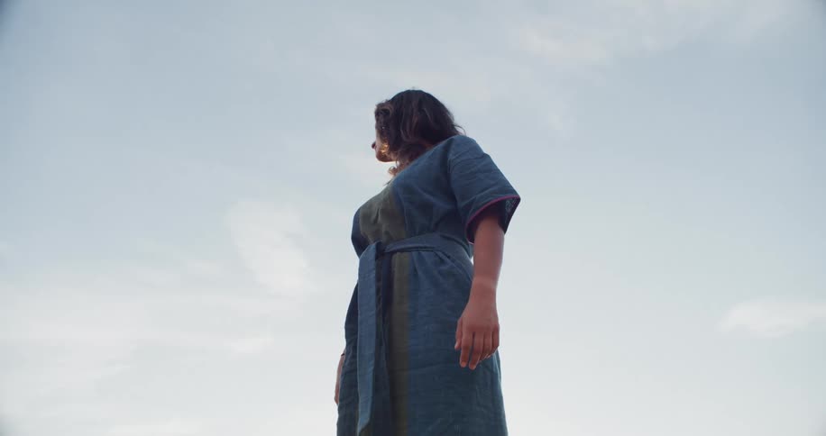 Woman wearing belted dress stands outdoors looking around