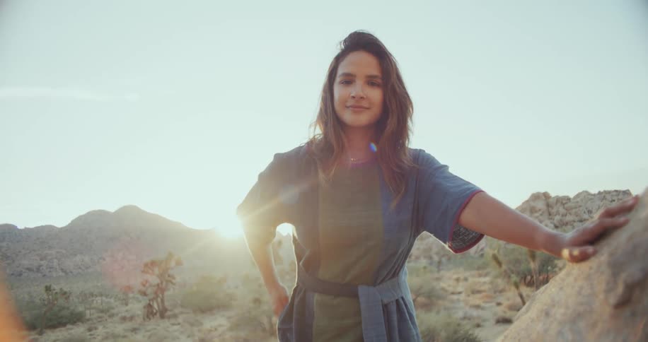 Latin woman standing outdoors touching a rock in a desert area at a sunny day
