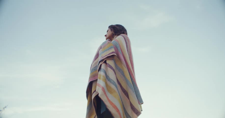 Woman standing outdoors wrapped in a colorful blanket during the day