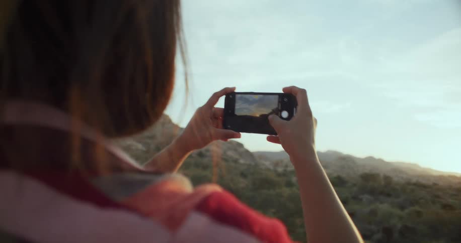 Woman standing near a forest taking pictures of the sunset ahead