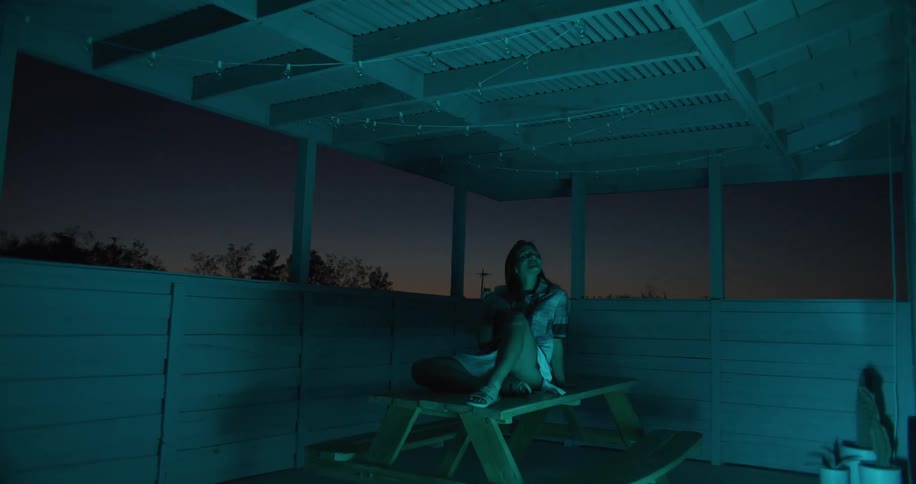 Woman sitting on the table at the houses balcony turning the hanging lights above her on and off while watching in awe